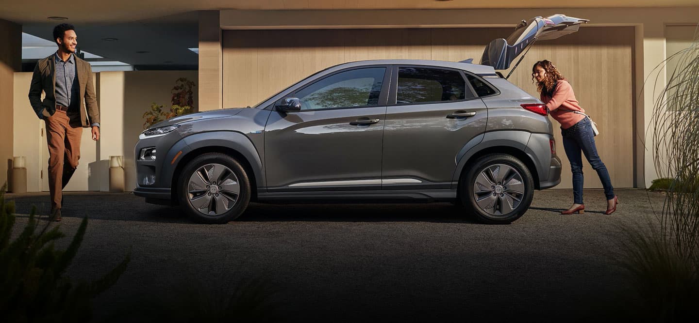 Grey Hybrid Vehicle sitting in the driveway while a women unloads the trunk